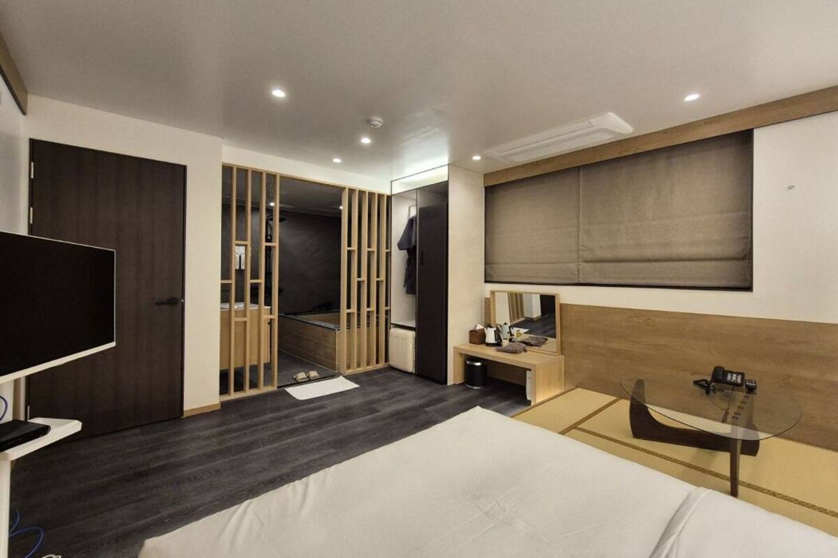 A modern hotel room with a large bed, a TV, a desk, and a walk-in closet.