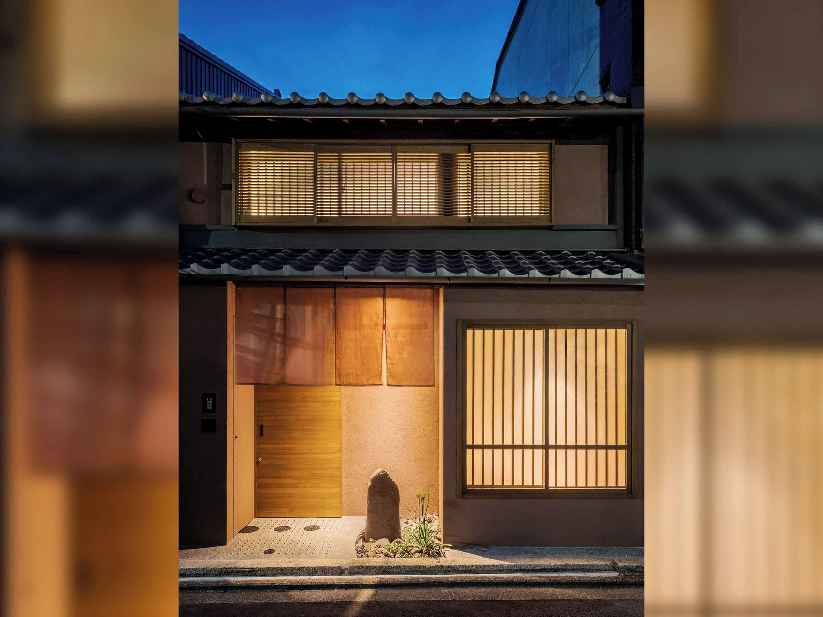 En traditionel japansk bygning med en trædør, en lille have og et stort vindue med lodrette skodder.