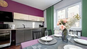 Une cuisine moderne avec un coin repas aménagé pour deux personnes, comprenant une horloge, un téléviseur à écran plat et un vase avec des fleurs.