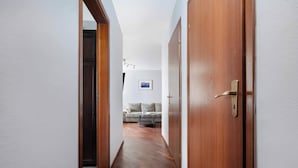 Un couloir doté de parquets et de portes donnant sur un espace de vie comprenant un canapé et une petite table.