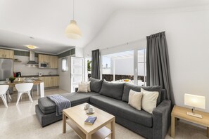 A modern living room with a grey sofa, a wooden coffee table, and a dining area with white chairs. - Casa Lago Verde - 2B (2) by Escape Home (Puerto del Carmen)