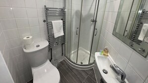 Et moderne badeværelse med toilet, bruseniche i glas, vask og spejl.