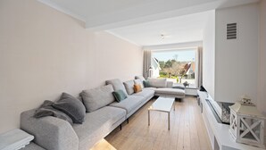 Un salon moderne avec un canapé d’angle gris, une table basse blanche et une vue sur l’extérieur.