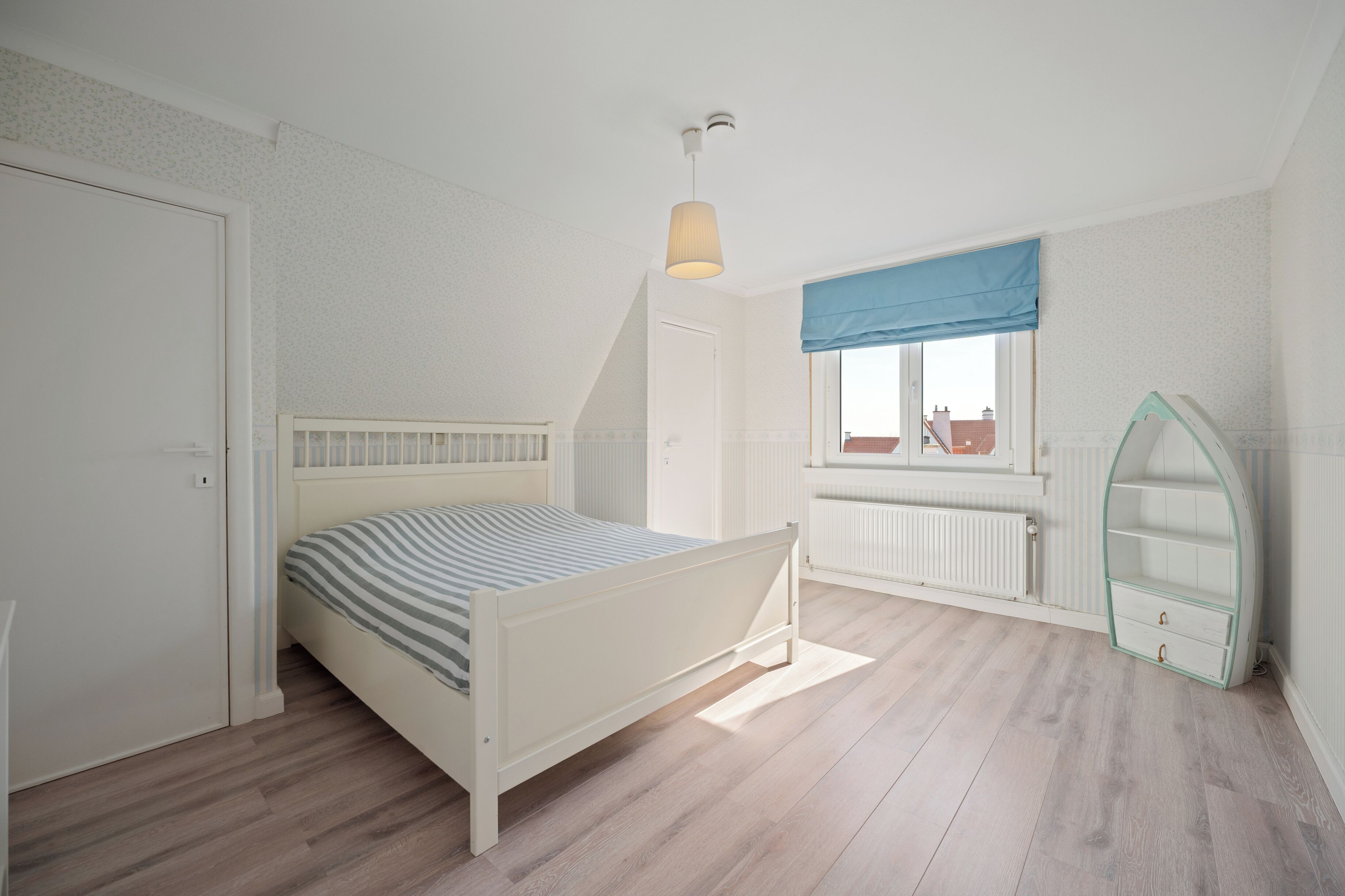 A bedroom with a bed, a window with a view, a radiator, and a curved shelf.