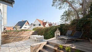 Un patio con mobiliario exterior, una terraza de madera y vistas a casas al fondo.