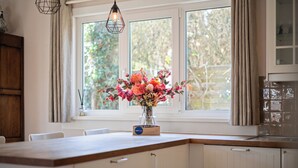 Une cuisine avec une grande fenêtre, un vase rempli de fleurs et un plan de travail en bois.