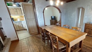 Un coin repas avec une table et des chaises en bois, une cuisine à l’arrière-plan et un sol carrelé.