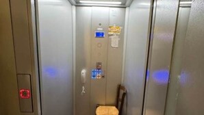 Un ascenseur avec un siège au centre, un panneau de commande à gauche et un panneau indicateur sur le mur.