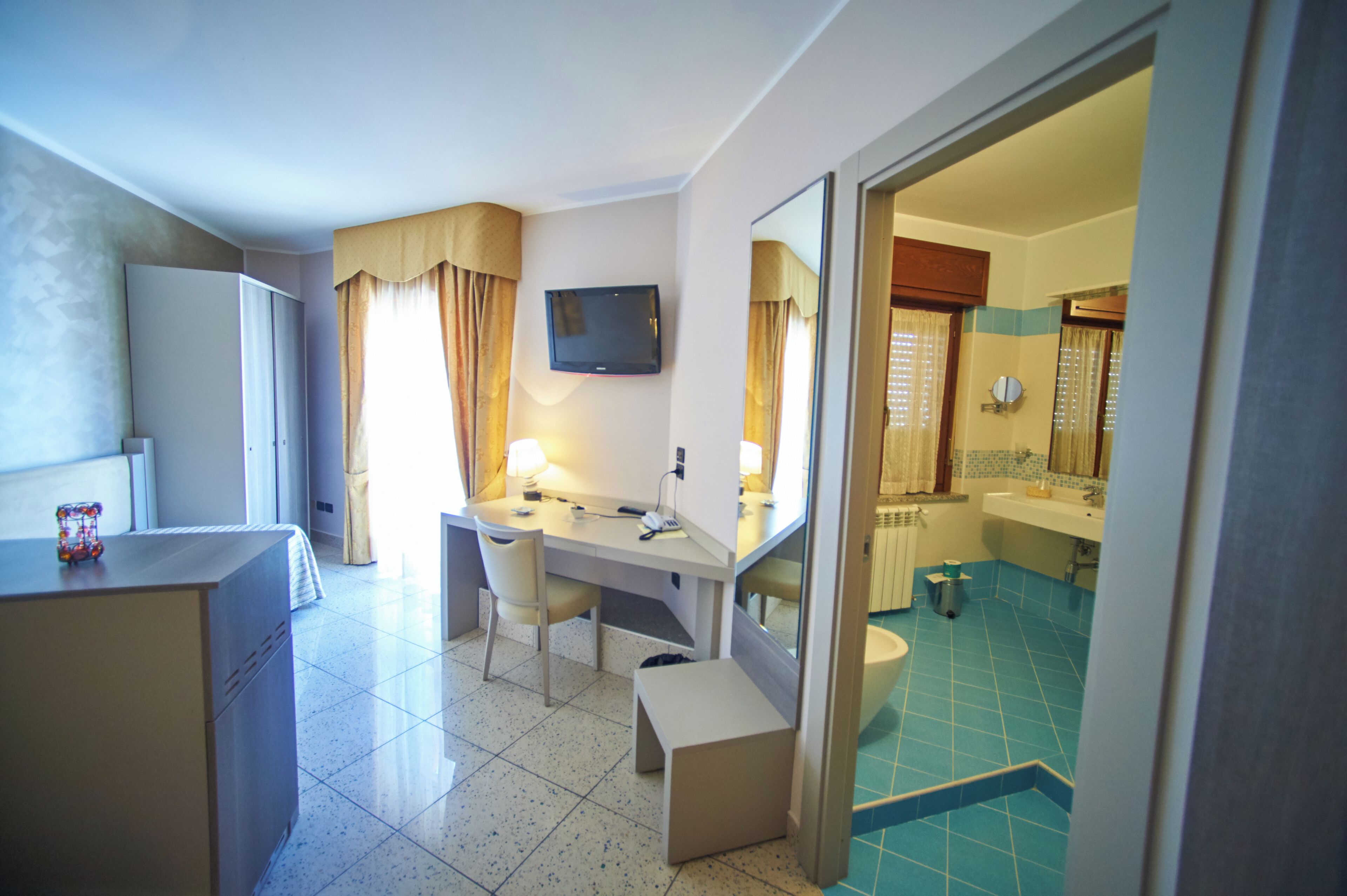 A hotel room with a desk, chair, and a television. There is a bathroom with a sink and a toilet visible through an open door.