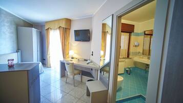 A hotel room with a desk, chair, and a television. There is a bathroom with a sink and a toilet visible through an open door.