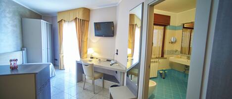 A hotel room with a desk, chair, and a television. There is a bathroom with a sink and a toilet visible through an open door.