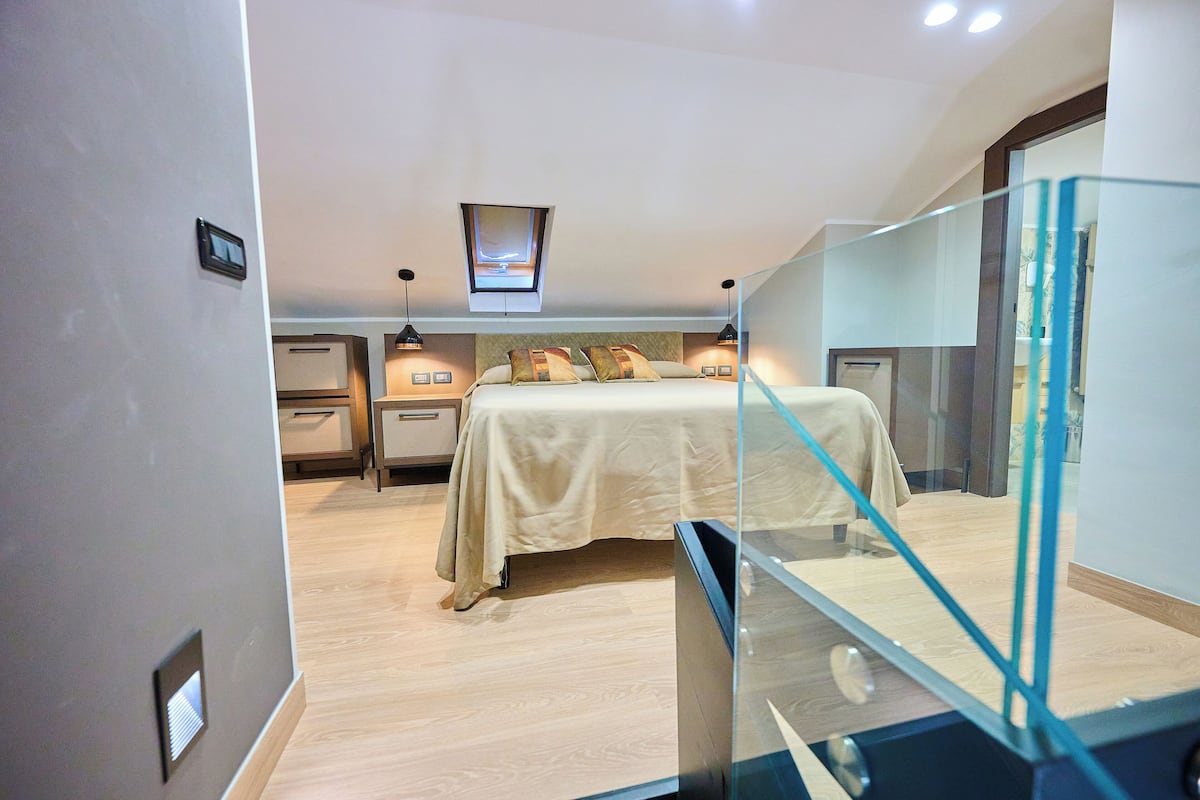 A bedroom with a bed, bedside tables, a ceiling light, and a glass railing.