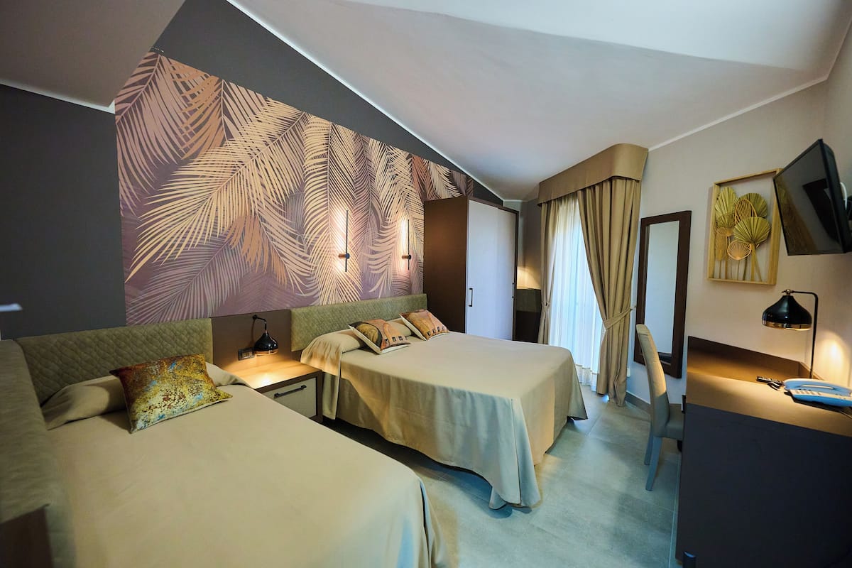 A hotel room with two beds, a desk, a chair, a TV, and a large wall mural.