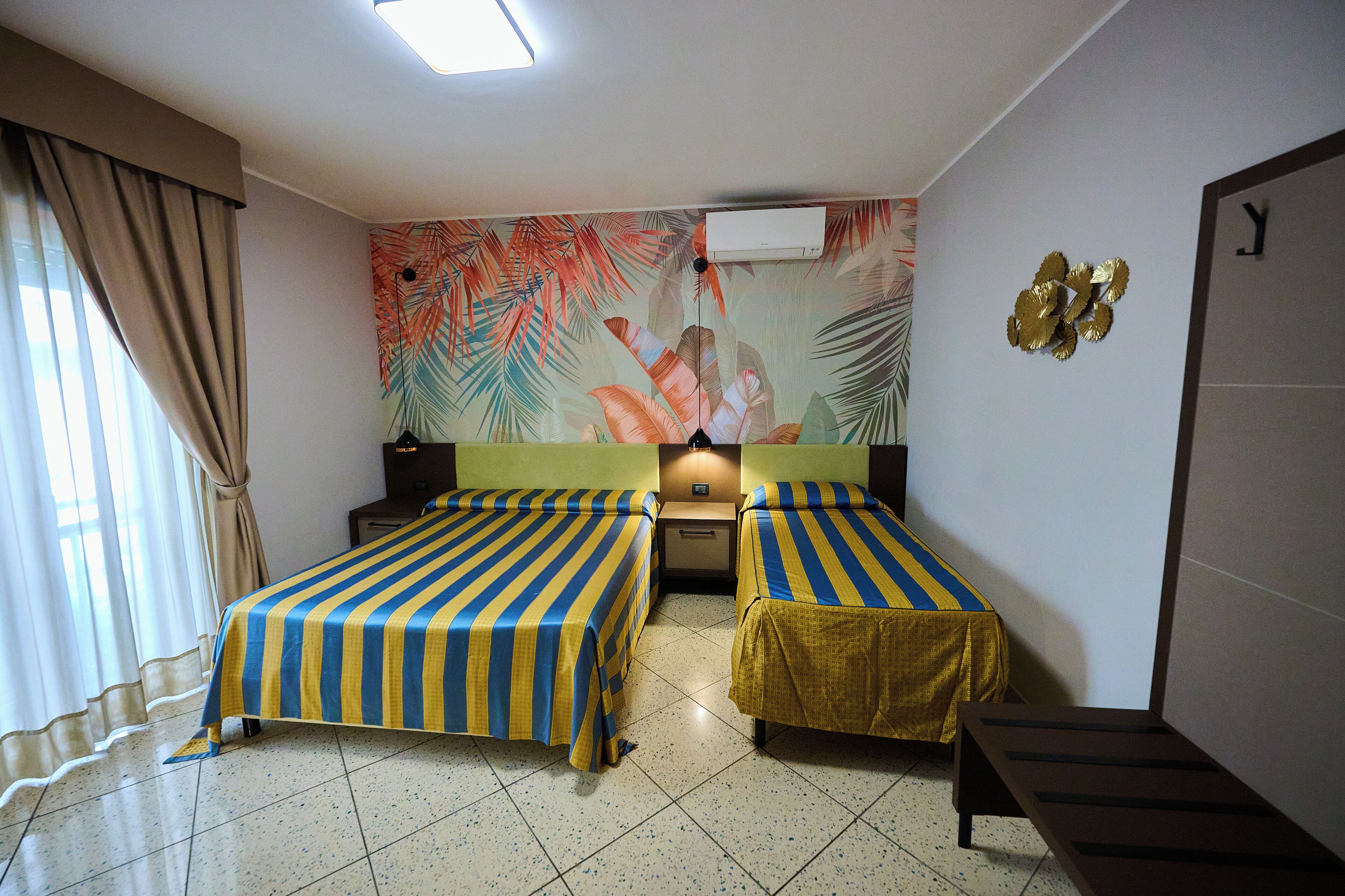 Habitación de hotel con dos camas, aire acondicionado de pared, mesita de noche y un banco.