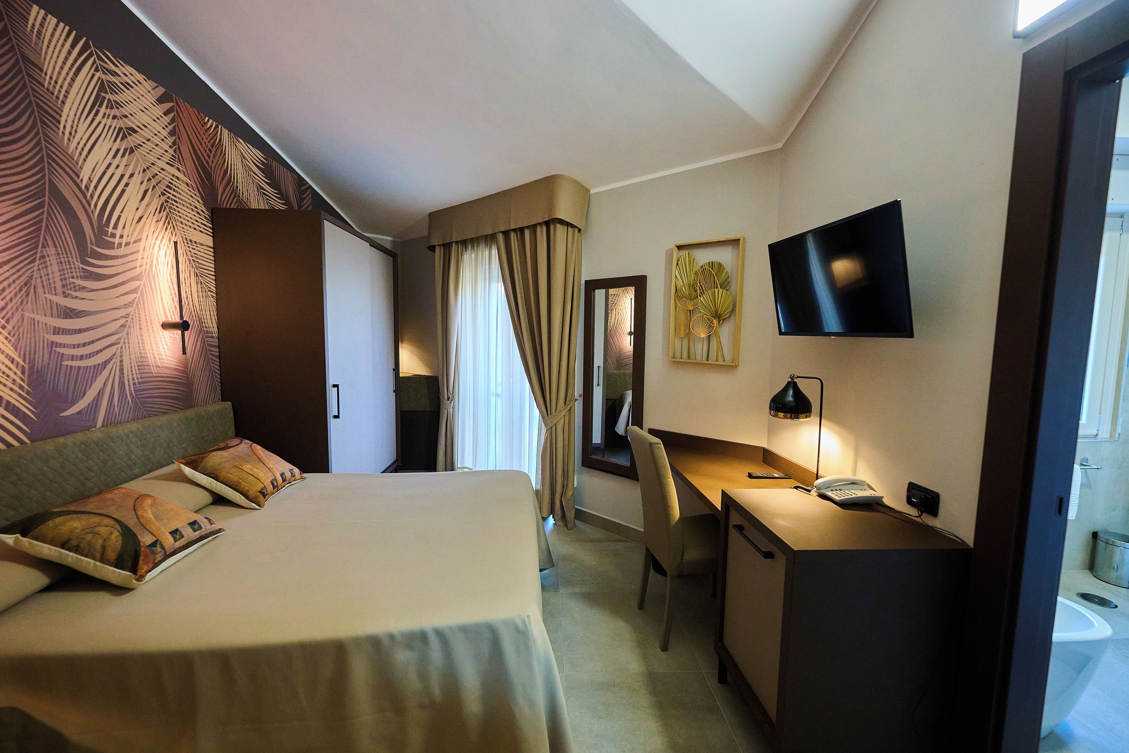 Ein Hotelzimmer mit Bett, Schreibtisch, Stuhl, Fernseher und einem durchgegangenen Tür sichtbaren Badezimmer.