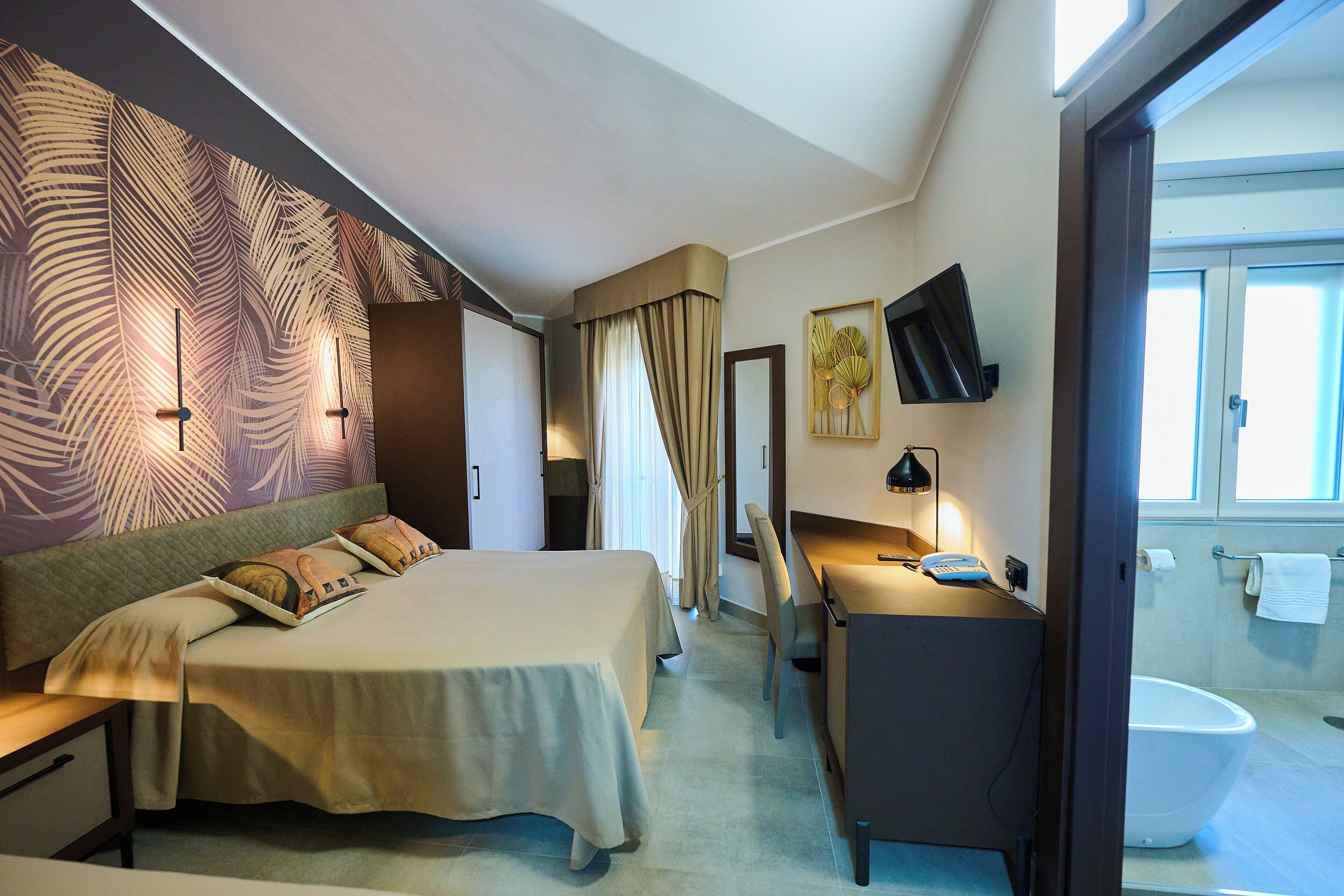 Habitación de hotel con cama, escritorio, silla y baño visible a través de una puerta abierta.