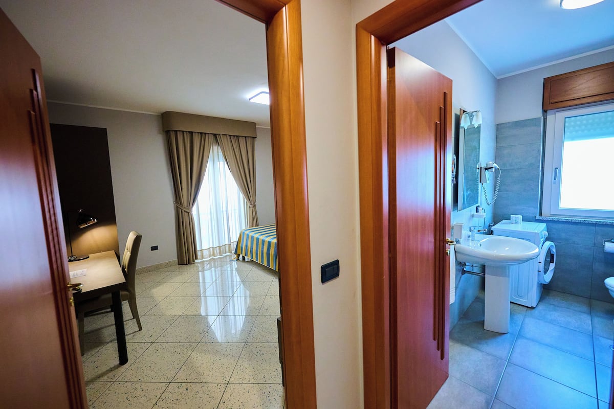 A hotel room with a bed, a desk, and a bathroom with a sink and washing machine.