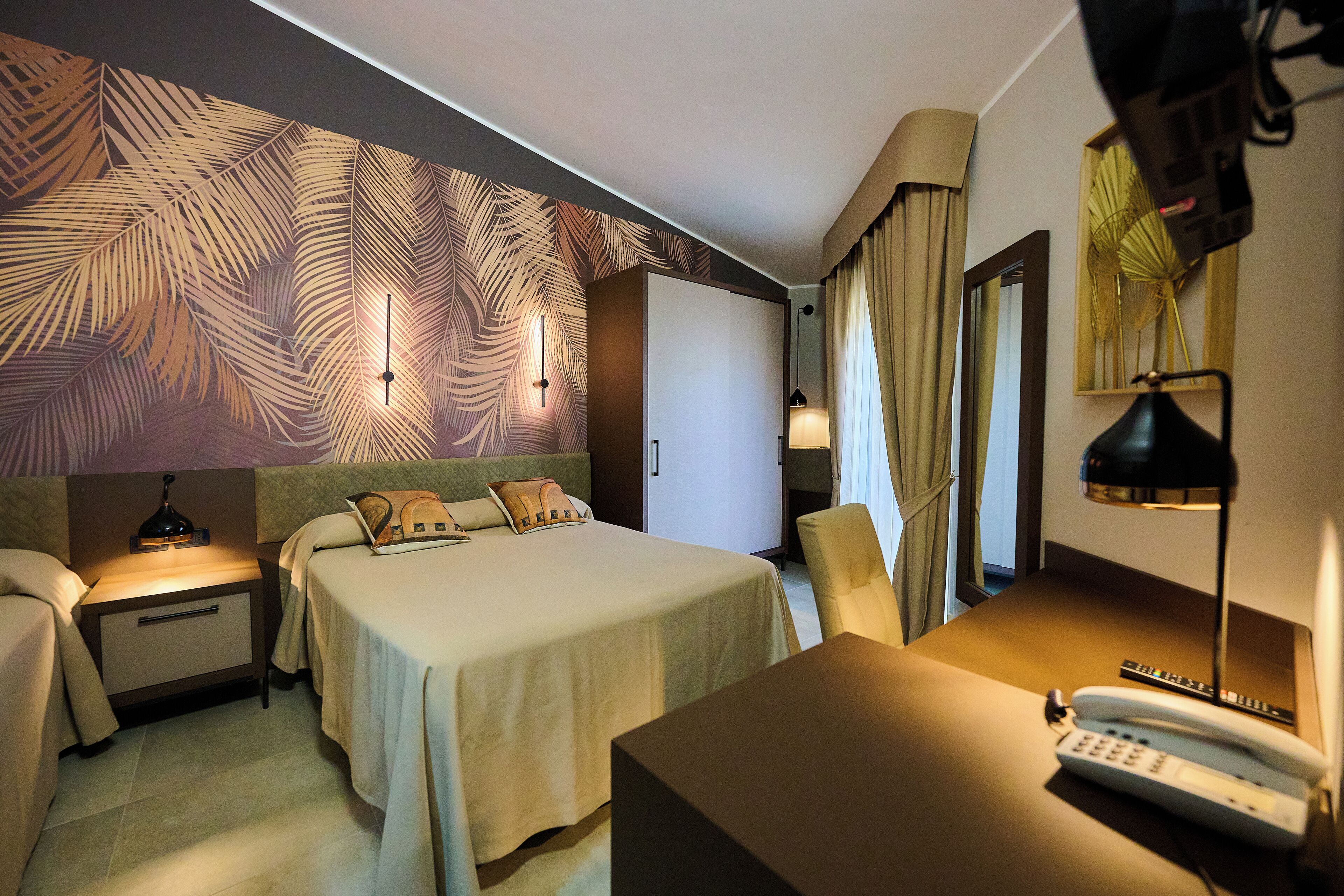 A hotel room with a bed, bedside tables, a desk with a phone, and a lamp.