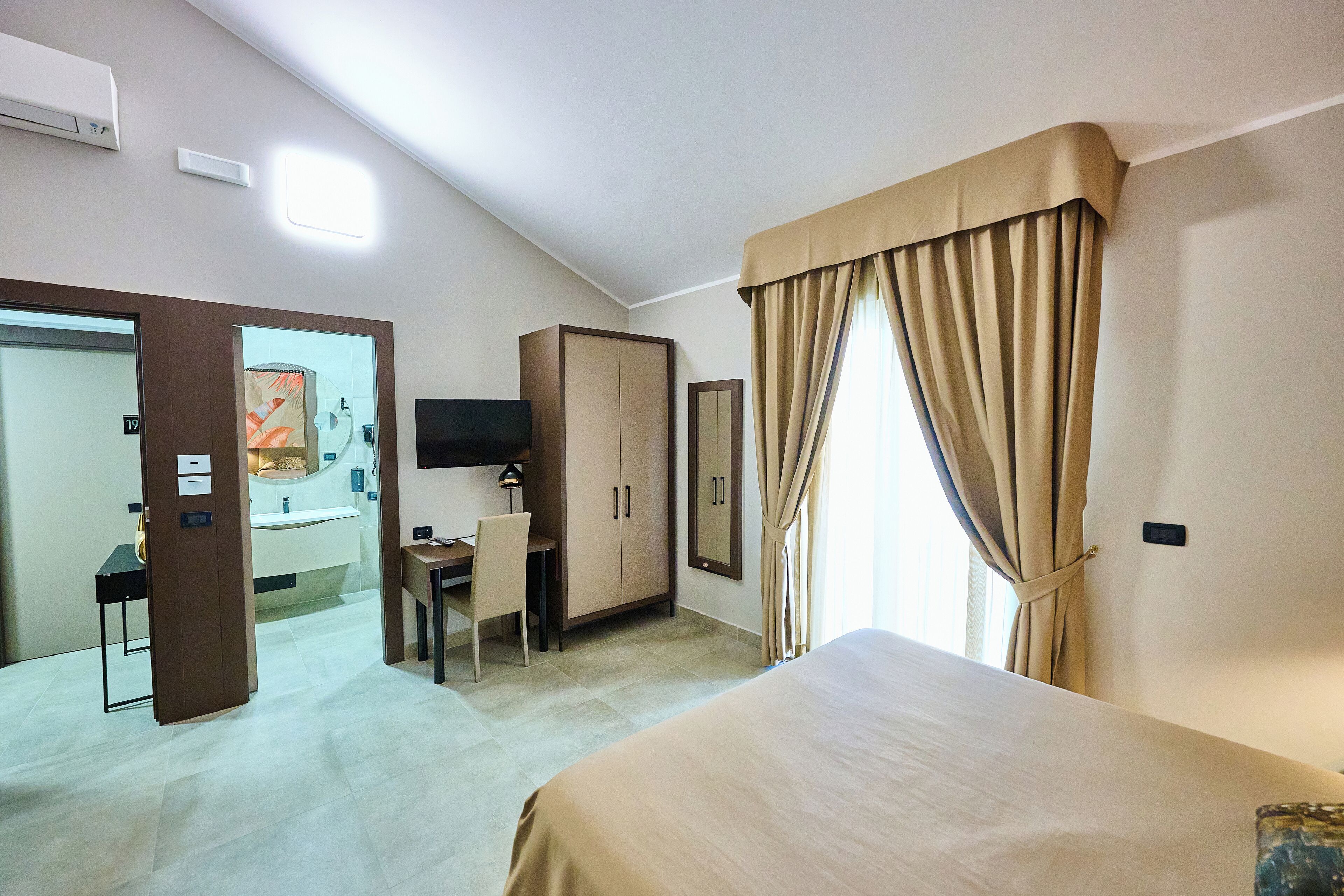 Una camera d'albergo con un letto, una scrivania, una sedia, un armadio e una televisione.