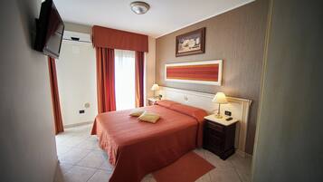 A hotel room with a bed, bedside tables, a TV mounted on the wall, and a window with curtains.