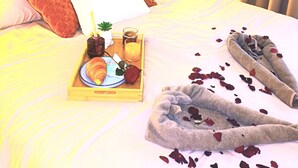 Ein Hotelzimmer mit Bett, Kissen, einem Tablett mit Frühstücksangeboten und Hausschuhen auf dem Bett.