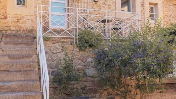A stone building with a white metal staircase leading to a balcony. There are two chairs and a small table in the foreground. - Cosy gîte for 6 people in the heart of the Fontfroide massif (Narbonne)