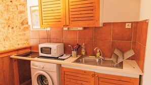 A compact kitchen with wooden cabinets, a washing machine, a microwave, and a sink. - Cosy gîte for 6 people in the heart of the Fontfroide massif (Narbonne)
