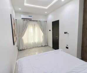 Ein Schlafzimmer mit Bett, einer Tür, einer Klimaanlage und einem Fenster mit Vorhängen.
