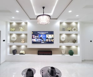 Ein modernes Wohnzimmer mit Flachbildfernseher, der Filmangebote zeigt, einer Kristallleuchtreiter und einem minimalistischen Design mit Regalen und Dekoration.