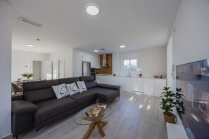 A modern living room with a sectional sofa, a glass coffee table, and a kitchen in the background. - Psicomagia Deluxe Villa by Fidalsa (Dolores)