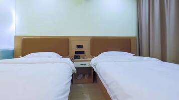 Habitación de hotel con dos camas individuales, cabecera de madera, mesita de noche con teléfono y reloj pequeño, y ventana con cortinas.