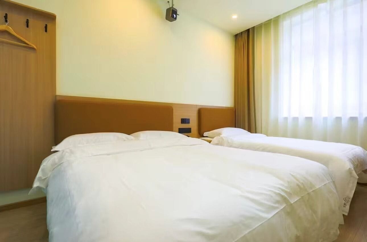 A hotel room with two beds, a wardrobe, and a window with curtains.