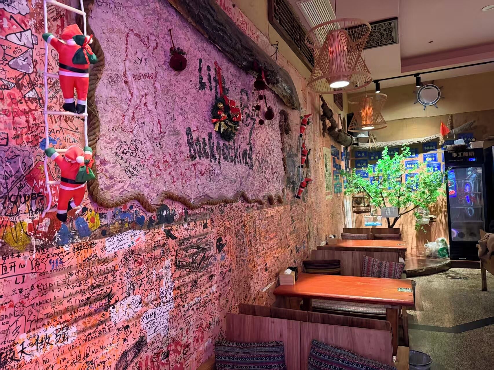 A restaurant with graffiti-covered walls, a wooden bench seating area, and a hanging decoration resembling a Santa Claus figure.