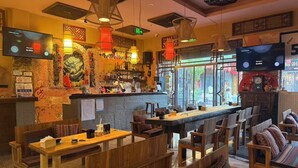 Eine gemütliche Bar mit Holzkubaturen, einer Bar und einer Theke mit verschiedenen Flaschen sowie einem Fernseher, der eine Sendung zeigt.