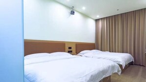 Ein Hotelzimmer mit zwei Einzelbetten, einem Holzkopfteil, einem an der Decke befestigten Projektor und einem großen Fenster mit Vorhängen.