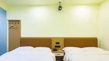 A hotel room with two beds, a wooden wardrobe, a small desk with a phone, and a wall-mounted light fixture.