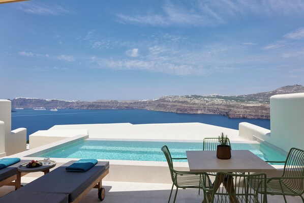 Zona de piscina con mesa y sillas, una bandeja con fruta y un vaso, y vistas al mar y acantilados.