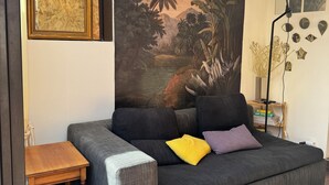 Un soggiorno con un divano grigio, un tavolino in legno e un grande murale tropicale sulla parete.