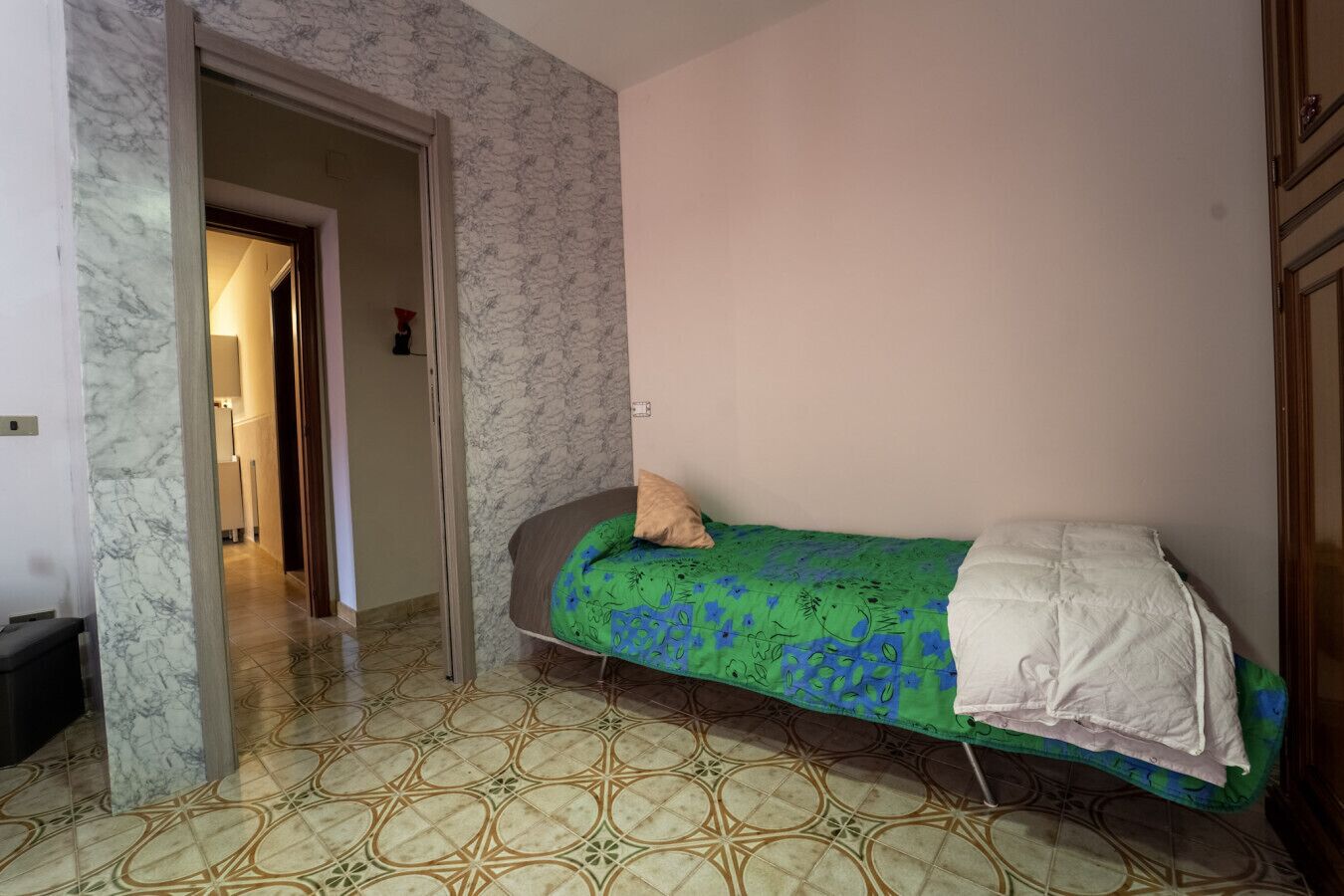 Ein Schlafzimmer mit einem Bett, einer Tür zu einem anderen Raum und einem gemusterten Boden.