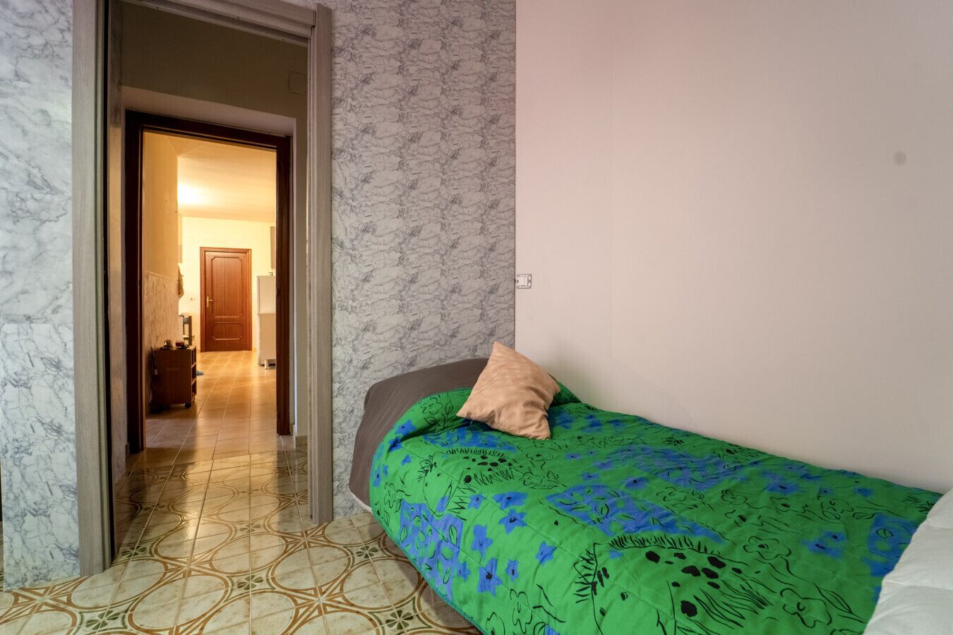 Une chambre à coucher avec une couvre-lit verte, un seul oreiller et un sol à motifs.