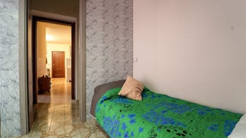 Une chambre à coucher avec une couvre-lit verte, un seul oreiller et un sol à motifs.