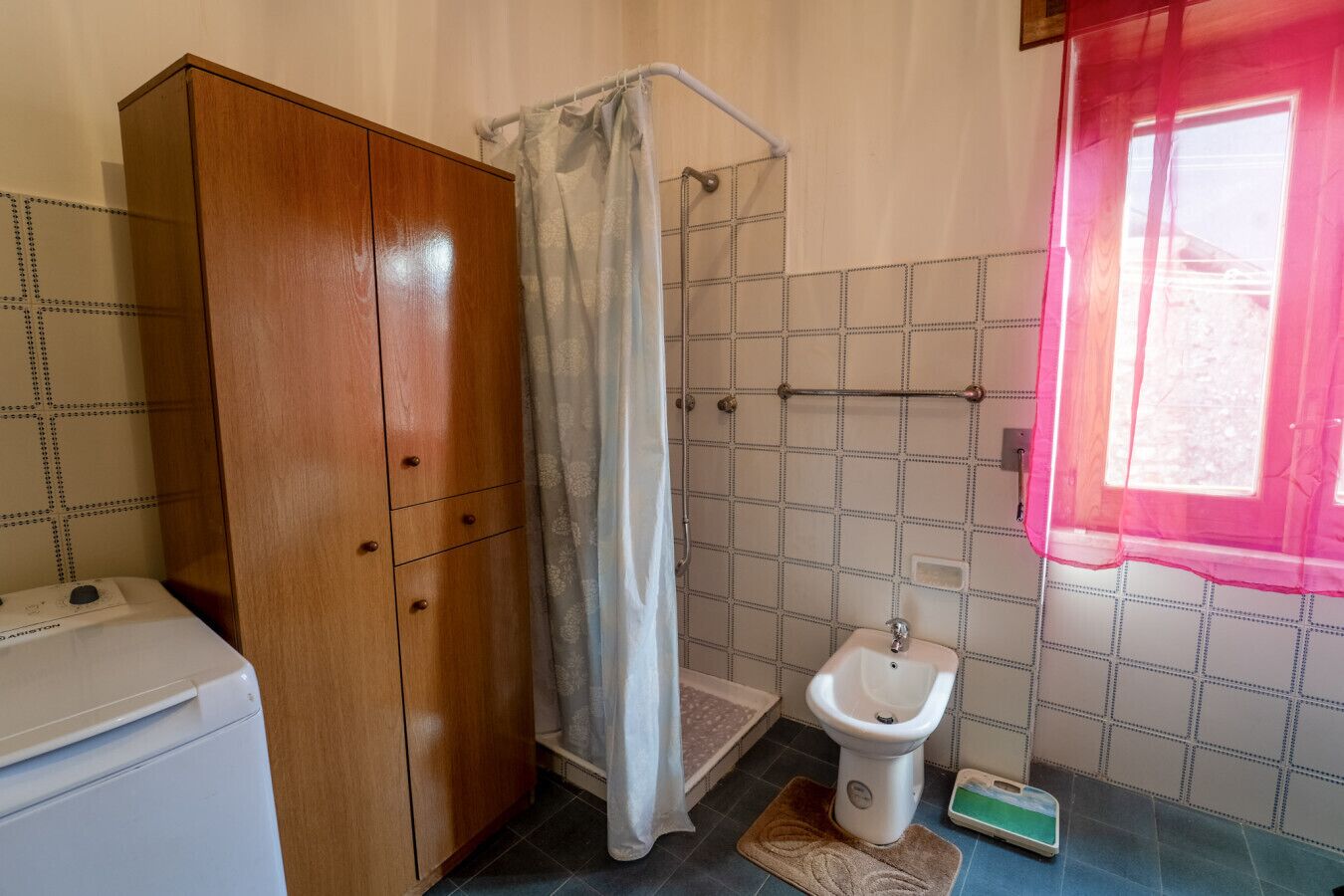 A small bathroom with a wooden wardrobe, a shower curtain, a toilet, and a sink.