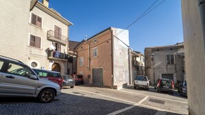 Una estrecha calle adoquinada flanqueada por edificios históricos, coches aparcados y un cielo azul despejado.