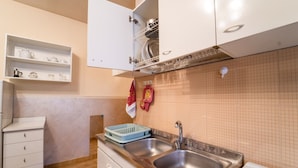 Una cocina con dos fregaderos, una encimera con escurreplatos y un armario blanco con estantes superiores.