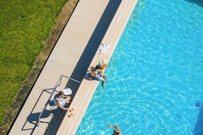 Ein Luftbild eines Schwimmbeckens mit Holzterrasse, Liegestuhl und kleinem Tisch.