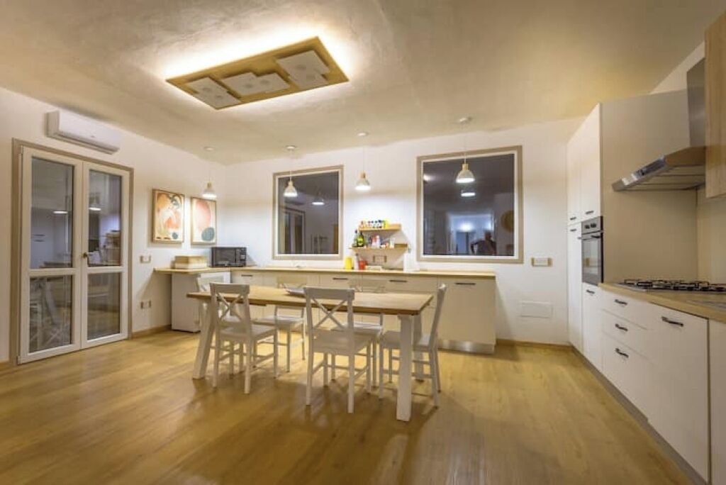A modern kitchen with wooden flooring, white cabinetry, and pendant lighting.