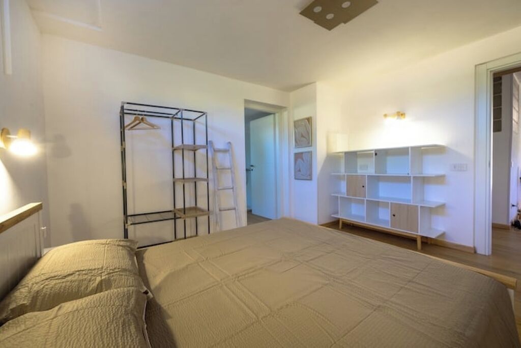 Un dormitori amb un llit, un armari, una estanteria i una porta que dona a una altra habitació.