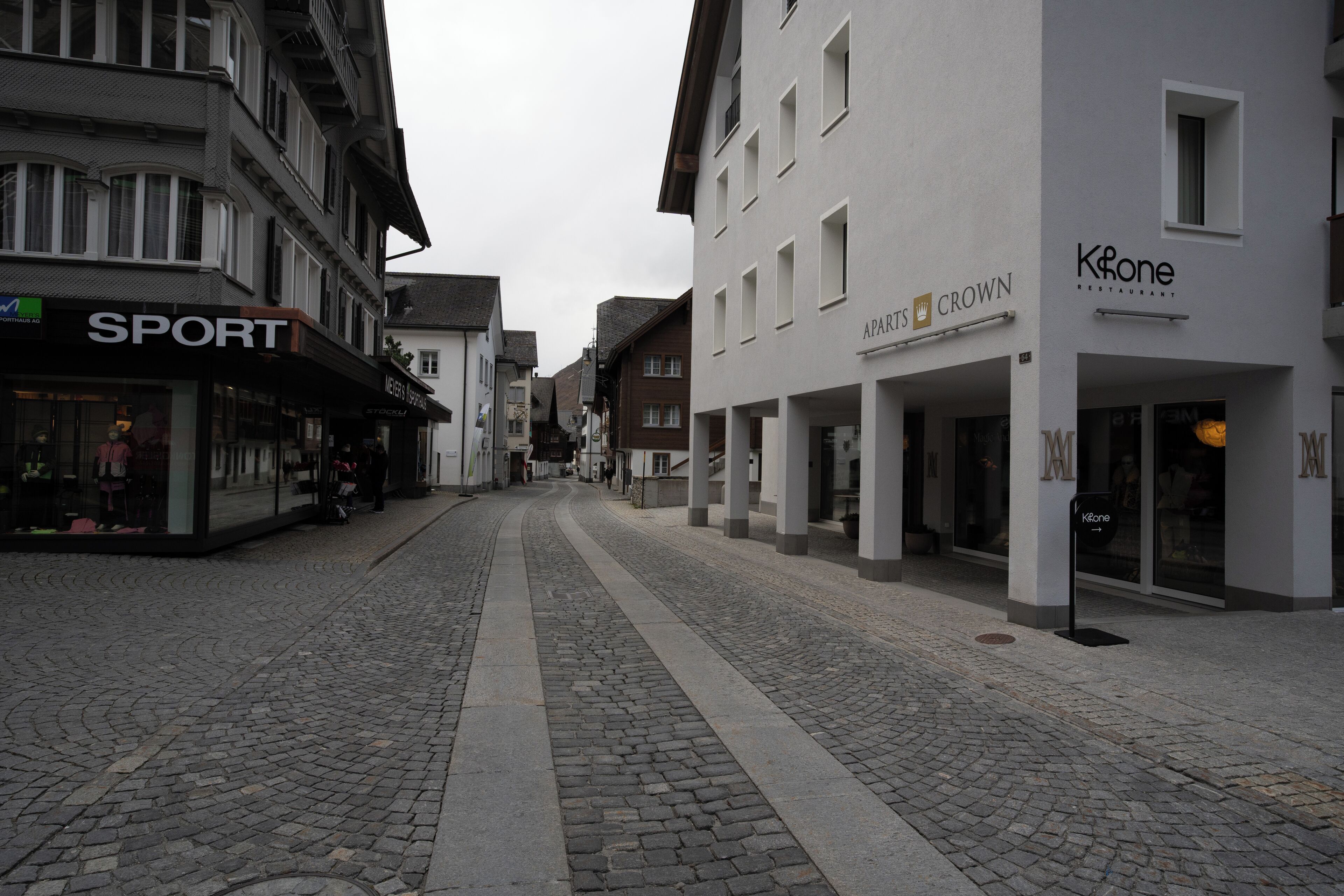 Une rue pavée bordée d’immeubles, dont un magasin de sport et un restaurant appelé « Crown ».