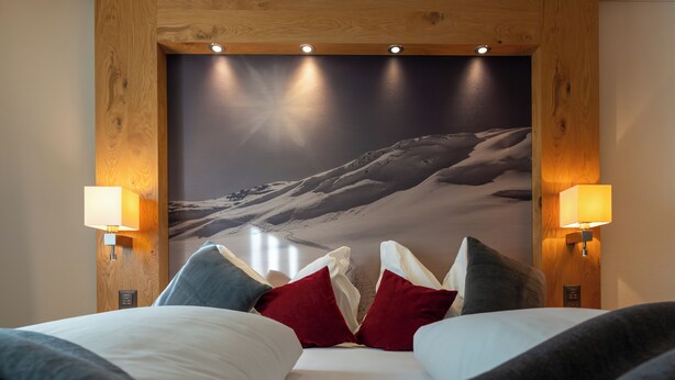 A hotel room with a bed, pillows, and a large wall mural of a snowy mountain.