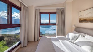 A hotel room with a large window offering a scenic view of mountains and a lake. - Lake Kremasta Hotel (Agrafa)